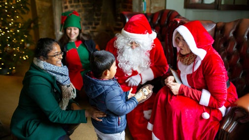 A mother and small child meeting Father Christmas, Mrs Claus and an elf at Scotney Castle, Kent